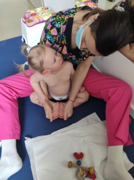 Fizjoterapeuta siedzi z dzieckiem na podłodze, widać zabawki dziecięce