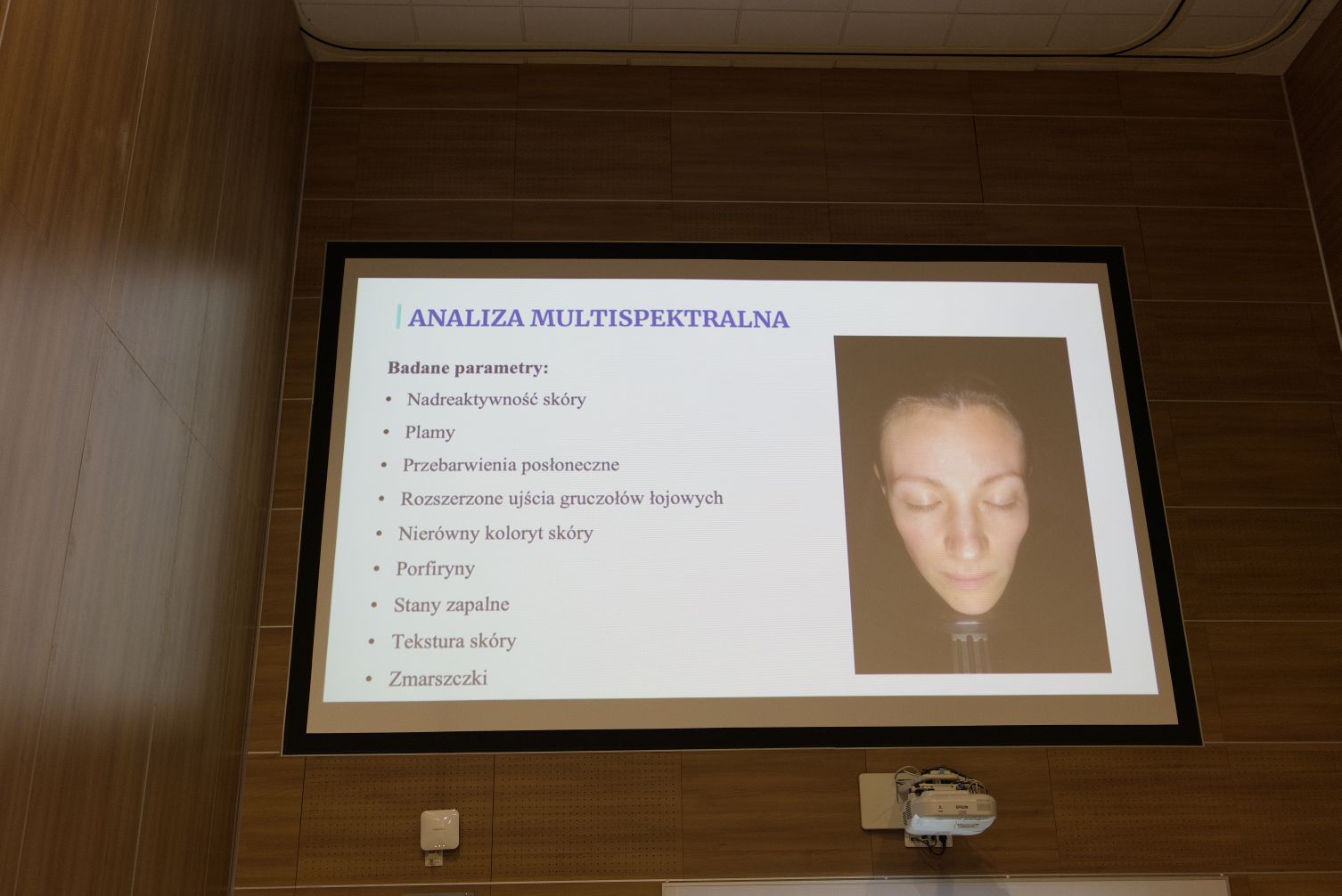 Na ekranie wyświetlany jest slajd prezentacji dotyczący analizy multispektralnej skóry. Materiał omawia wybrane parametry wykorzystywane w diagnostyce i ocenie kondycji skóry, a ilustracją jest zdjęcie twarzy wykonane podczas badania. Prezentacja stanowi element wykładu lub szkolenia z zakresu kosmetologii, dermatologii lub nowoczesnych metod diagnostycznych.